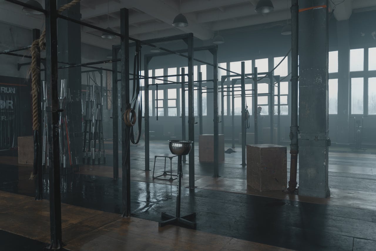hero-img Moody gym interior featuring various workout equipment like pull-up bars and ropes in a spacious industrial setting.